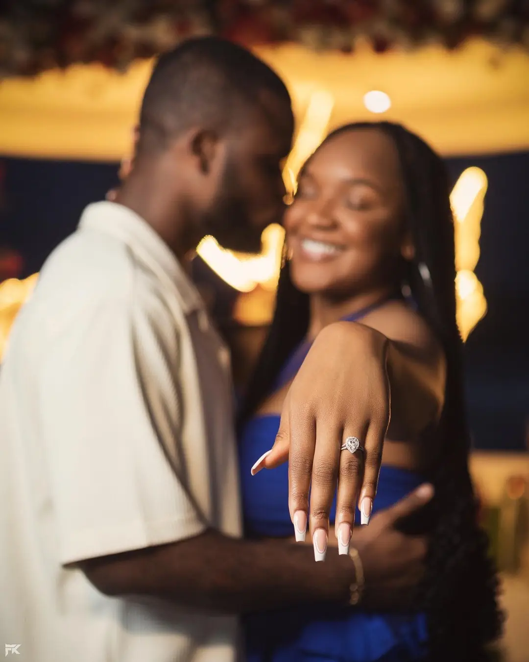 A woman showing her engagement ring, her partner kissing her cheek
